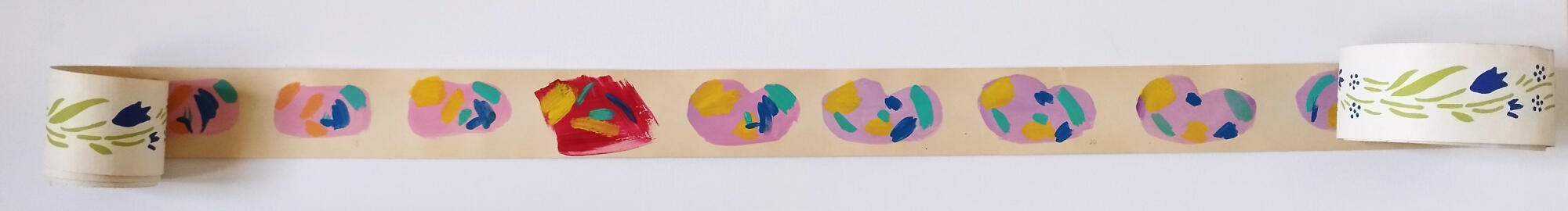 A photo of a roll of wallpaper. The wallpaper roll is opened and the inside has been painted with pink blobs. Inside the blobs are abstract and colorful shapes.